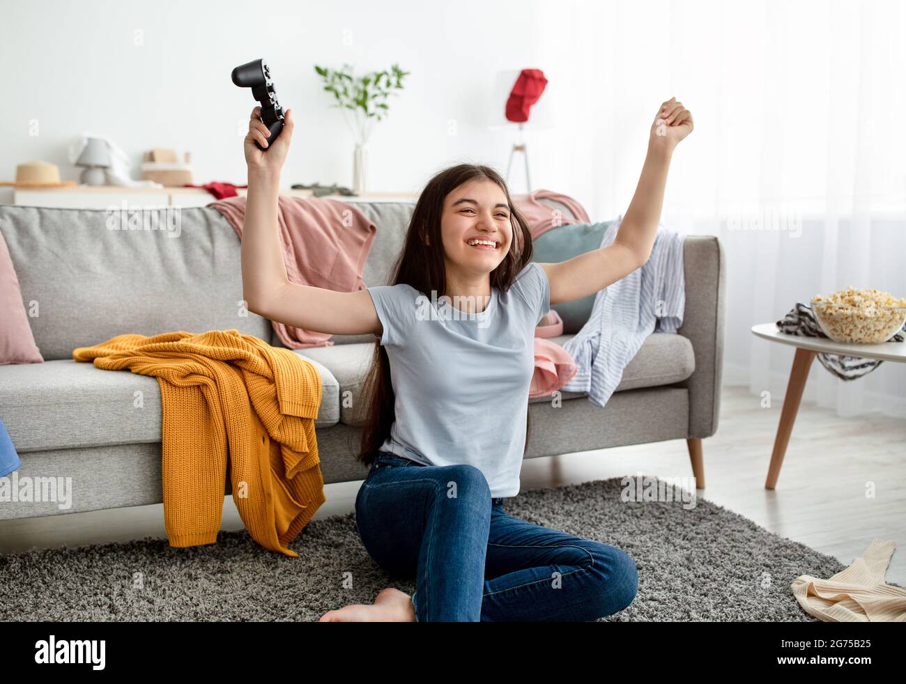 Happy Indian teen girl winning videogame on playstation, having fun, celebrating victory indoors Stock Photo