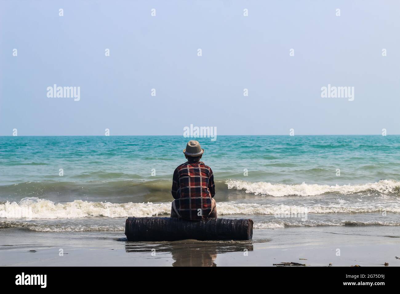 Rear view of a young man sitting on sand beach during sunrise ...