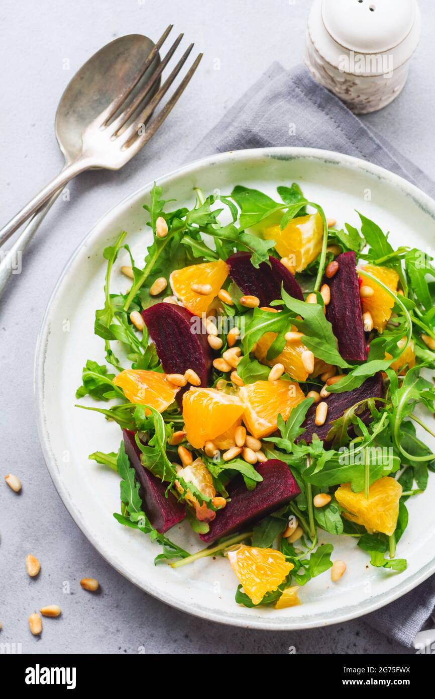 Salad of arugula, baked beetroot, orange and red onions with spices and pine nuts in awhite dish. Olive oil and ingredients on grey stone table. Selec Stock Photo