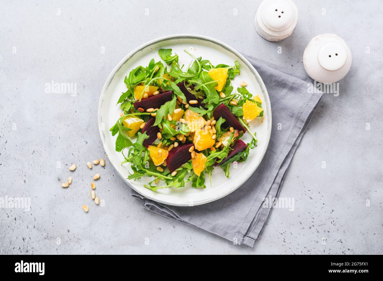 Salad of arugula, baked beetroot, orange and red onions with spices and pine nuts in awhite dish. Olive oil and ingredients on grey stone table. Selec Stock Photo