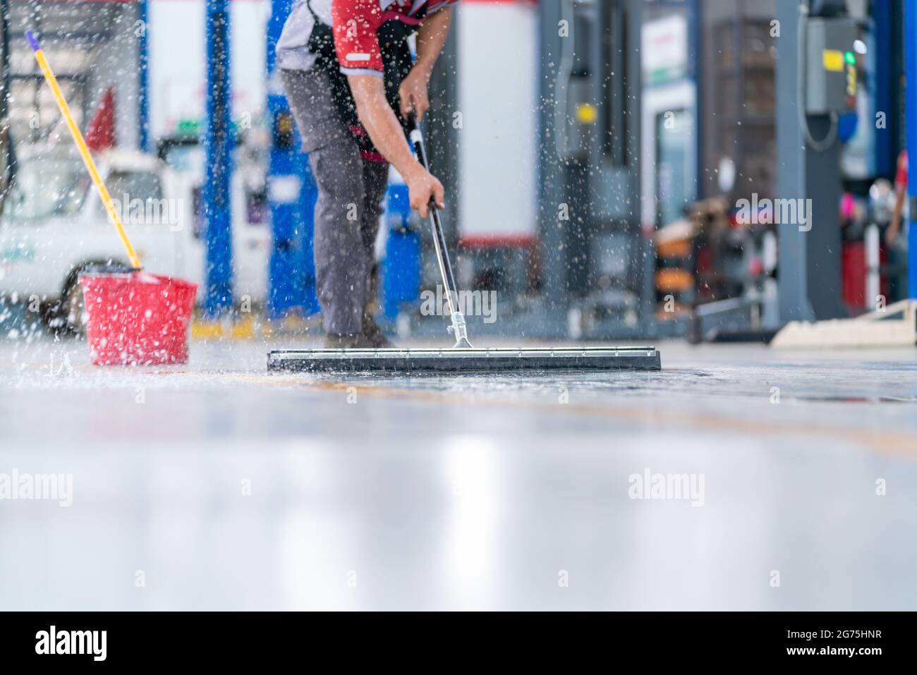service staff man using a mop to remove water in the uniform cleaning the protective clothing of the new epoxy floor in an empty warehouse or car serv Stock Photo