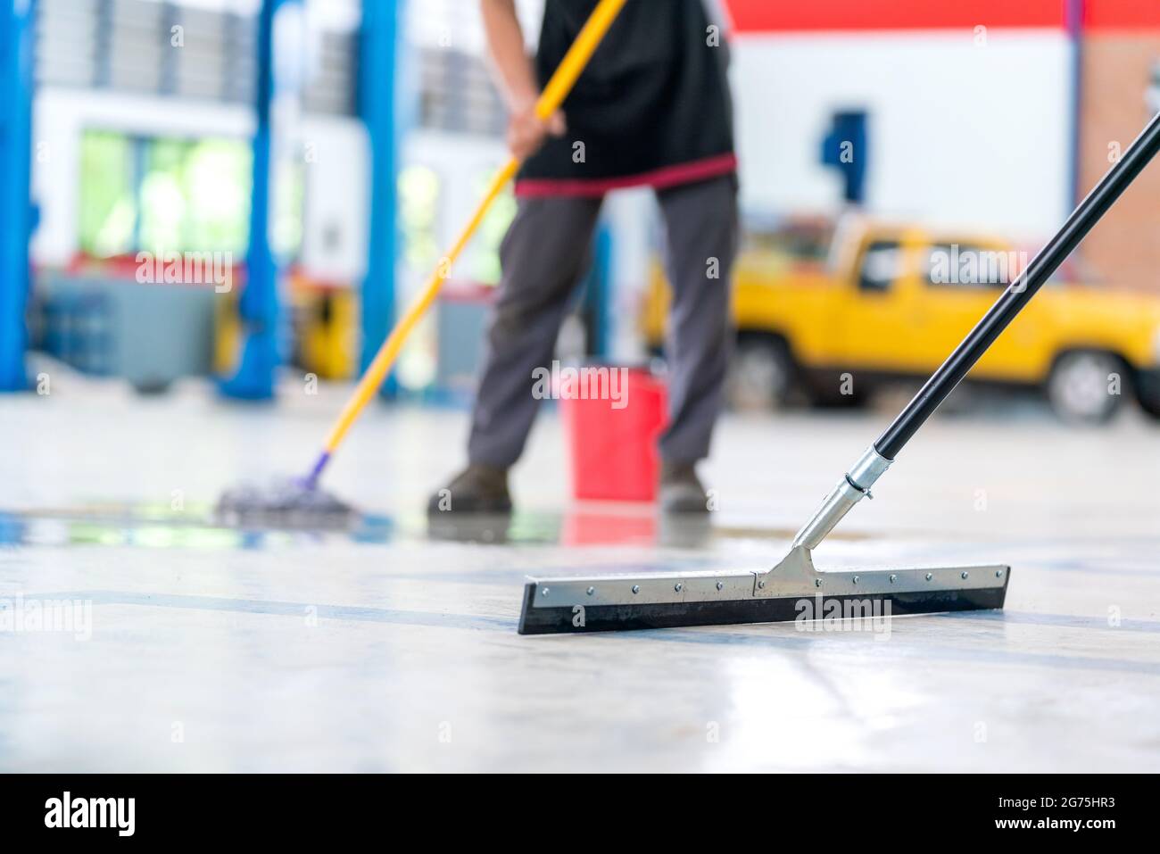 Select the focus mop, service staff man using a mop to remove water in the uniform cleaning the protective clothing of the new epoxy floor in an empty Stock Photo