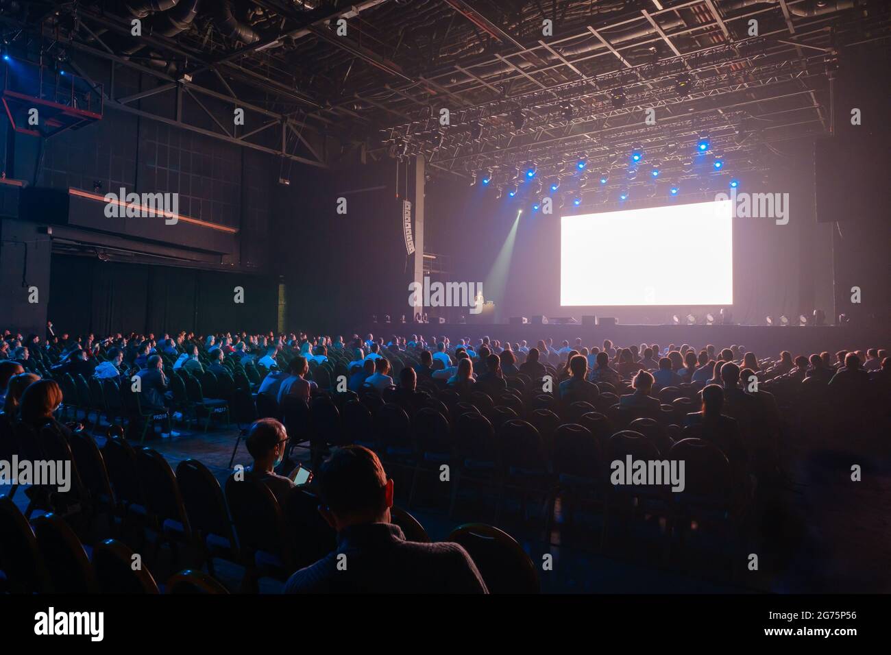 Audience sitting in front of stage with screen Stock Photo Alamy