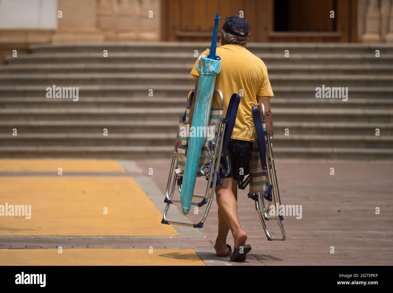 Malaga, Spain. 11th July, 2021. A man is seen carrying an umbrella and folding chairs as he walks in a square during a hot summer day at Rincon de la Victoria.Spain live its first heat wave with high temperatures near 45º degrees in many cities of the country, according to the Spanish Meteorological Agency. Spaniards take advantage of beaches to cool off at the Mediterranean Sea and enjoy good weather. (Photo by Jesus Merida/SOPA Images/Sipa USA) Credit: Sipa USA/Alamy Live News Stock Photo