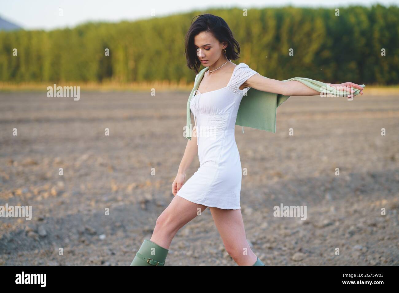 Asian woman, walking in the countryside, wearing a white dress and green wellies. Stock Photo