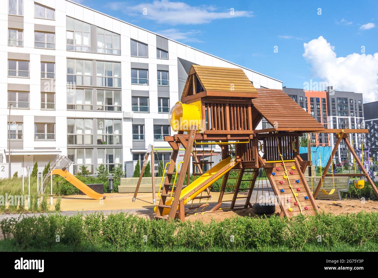 Modern wooden empty playground with swings, slides and climbing wall near residential apartment building Stock Photo