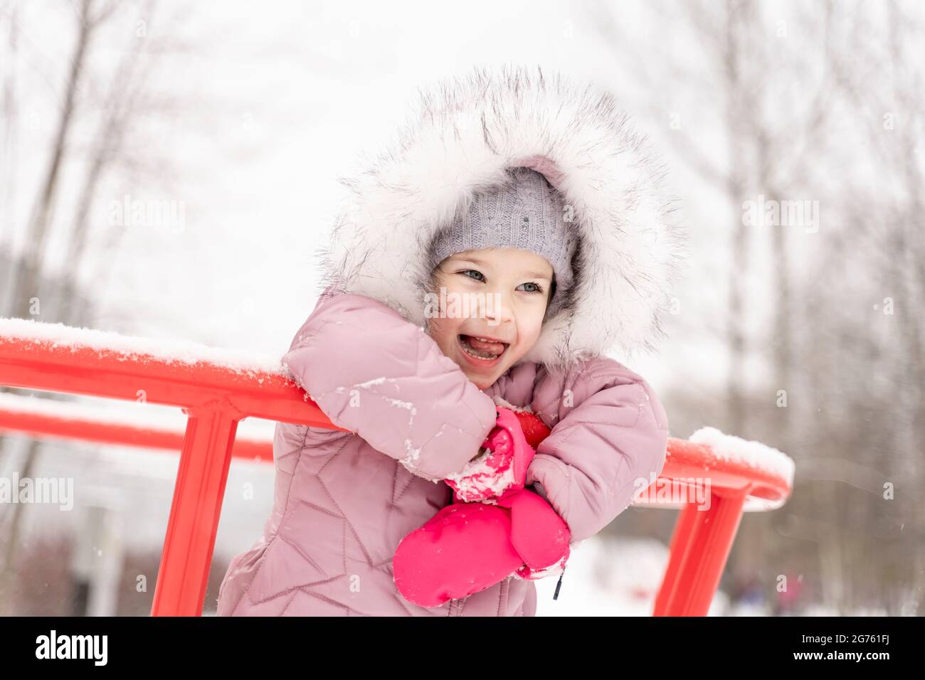 playful child girl in pink coat having fun in winter park Stock Photo