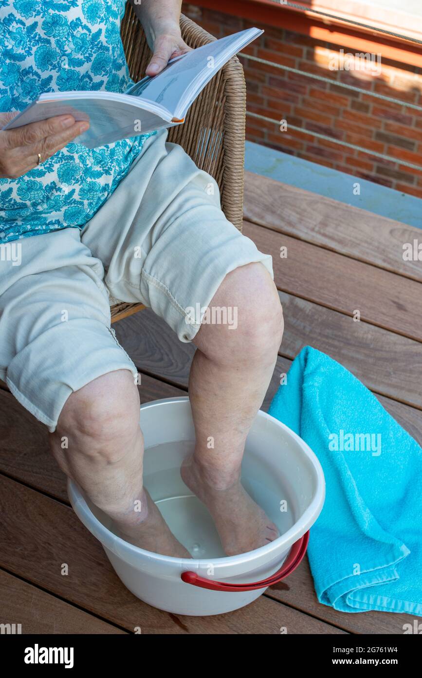 Senior woman relaxing reading book and soaking feet in the cold water