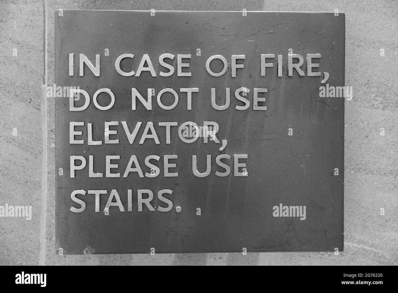A sign that says, In Case Of Fire, Do Not Use Elevator, Please Use Stairs, which direct people of what to do in case of an fire emergency. Black and W Stock Photo
