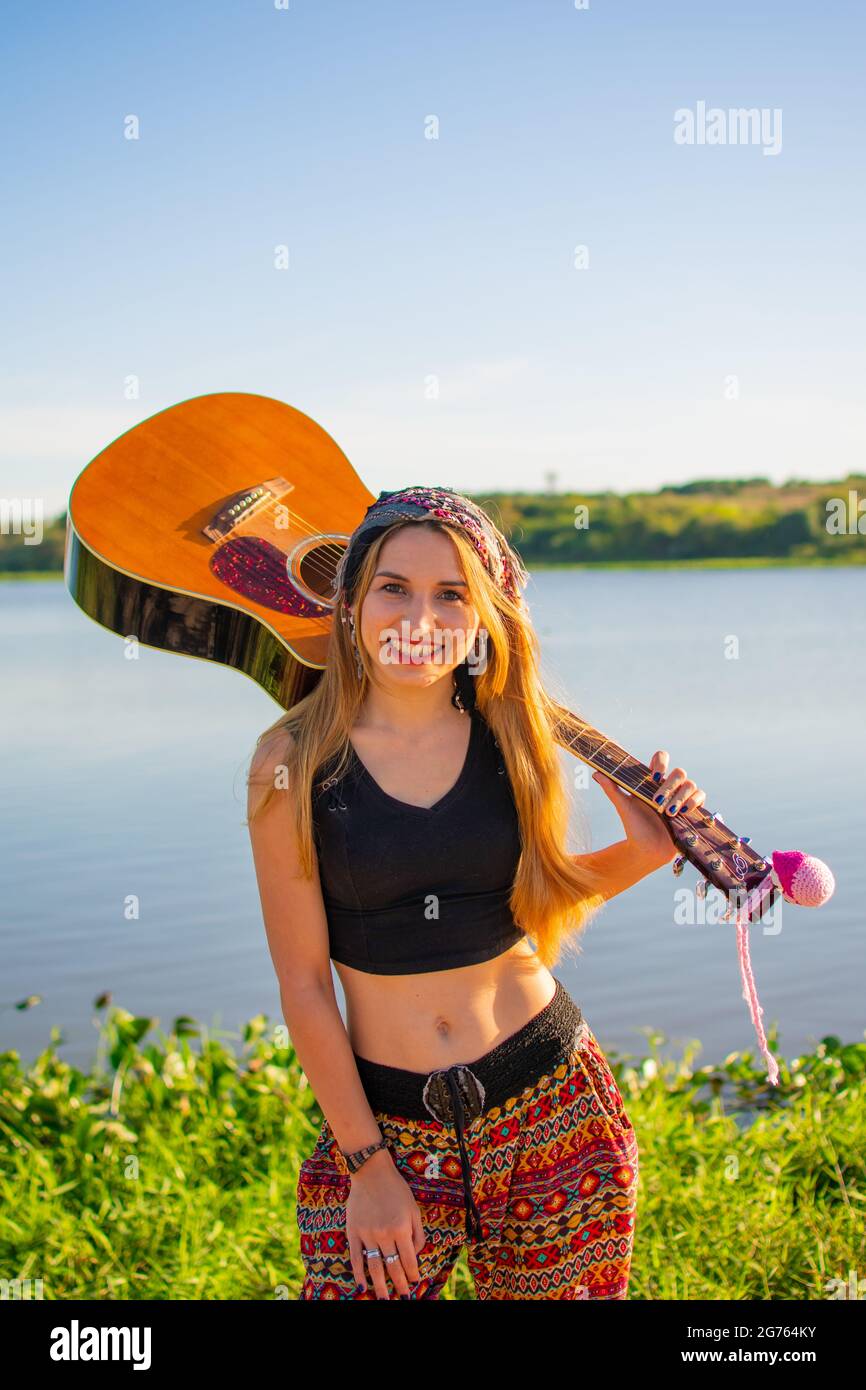 A pretty blonde Argentinian woman with a guitar on her shoulder posing