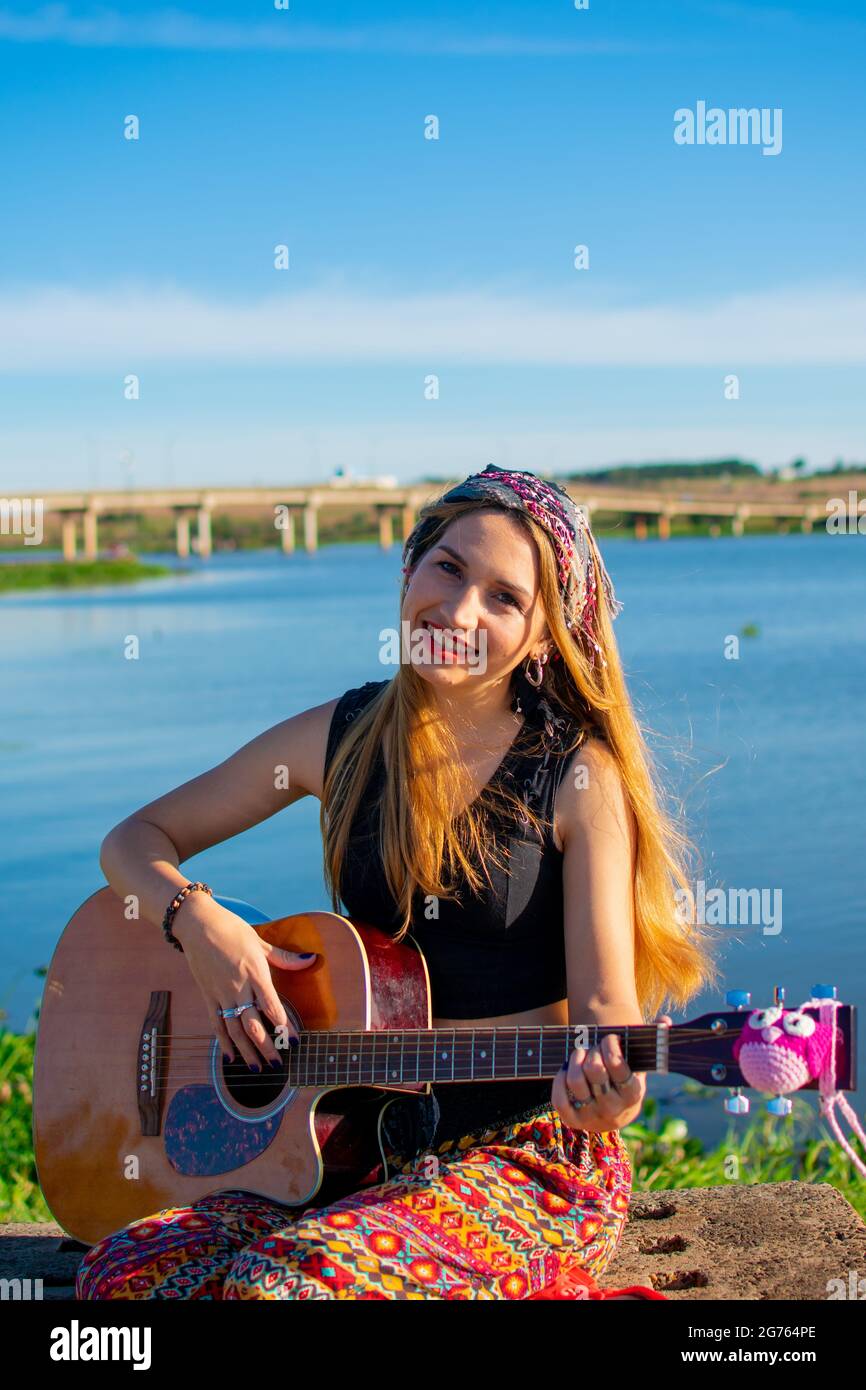 A pretty blonde Argentinian woman sitting on a bench with a guitar on