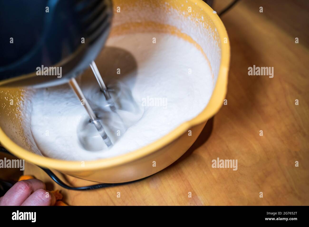 Mixing whipping cream in bowl with motor mixer on a wooden table in a