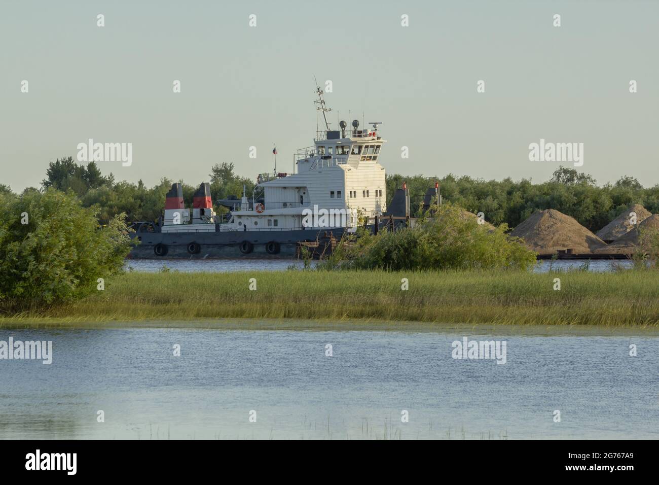 Transportation of building materials on the river. Dry cargo ship pushes a barge with sand along the river. Stock Photo