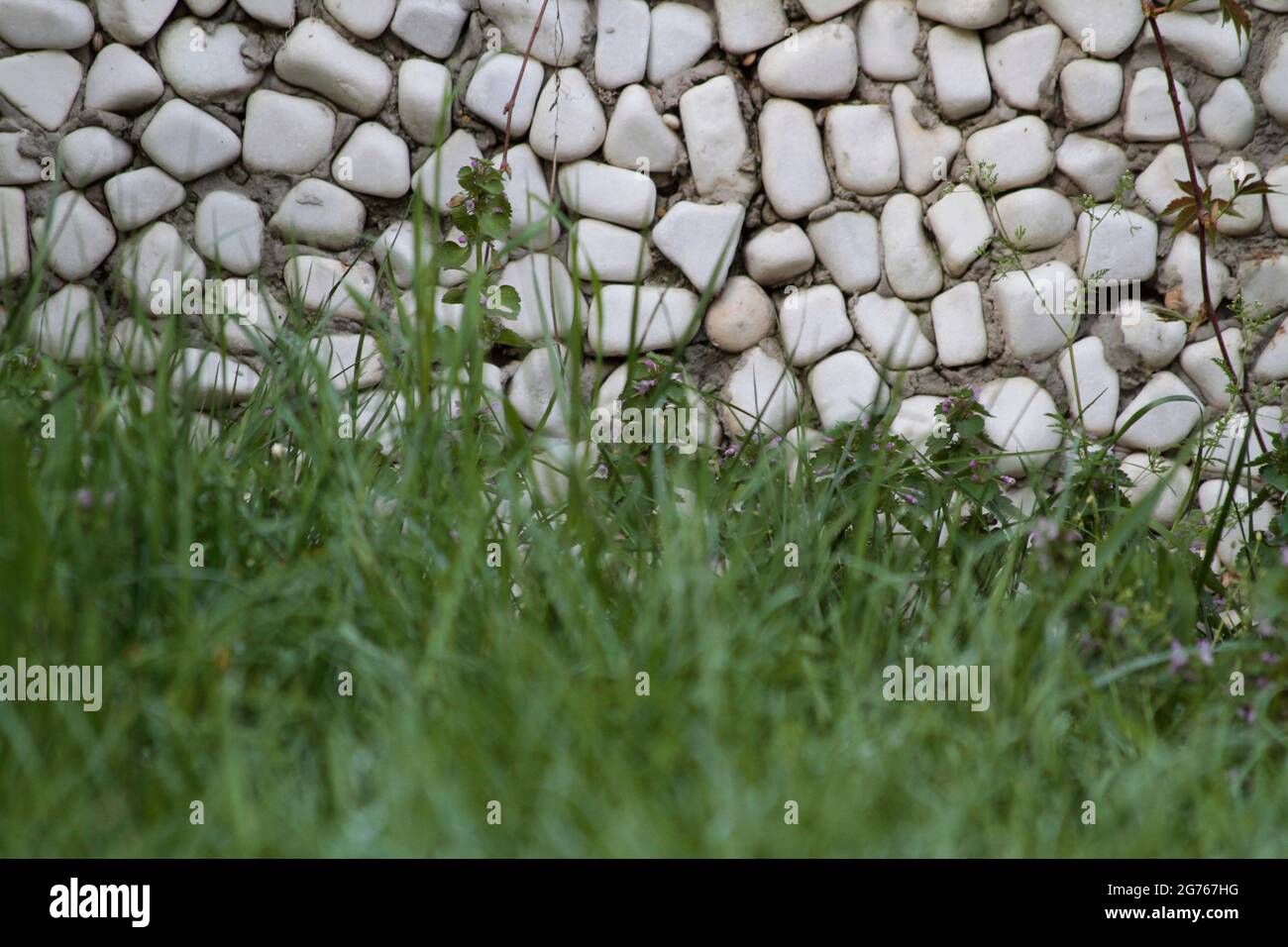 Wall cladding made using white, rounded white stones and grass. Wall cladding made using rounded stones. Stock Photo