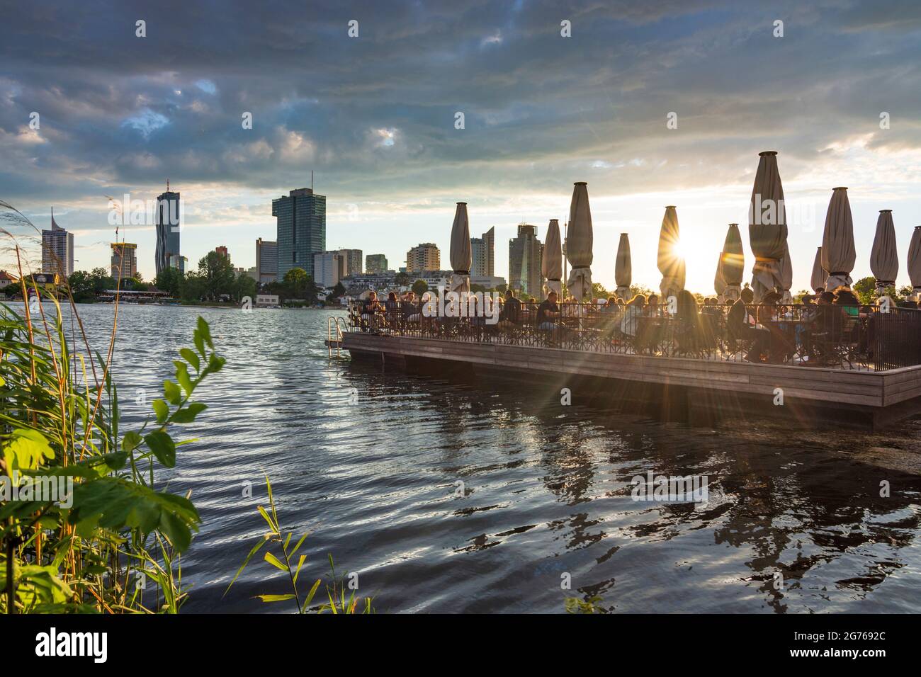Wien, Vienna: late sun at river Alte Donau (Old Danube), floating platform of restaurant Strandcafe, boats, tower Donauturm, highrises of Donaucity, D Stock Photo