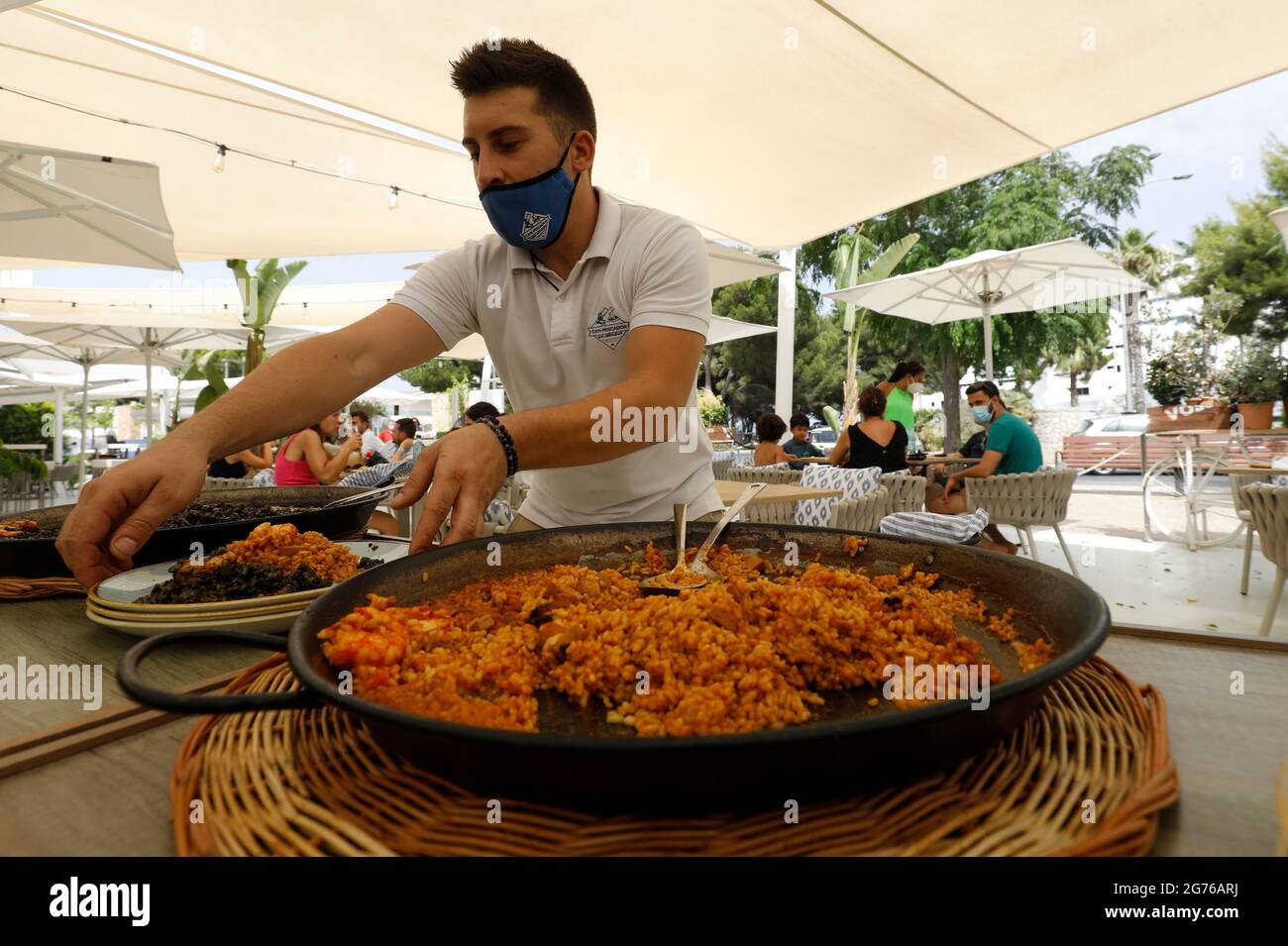 Spain. 11th July, 2021. The waiter Sebastian serves a paella in the restaurant Can Pescador on the beach Playa de Muro in the north of Mallorca. The federal government has declared the whole of Spain with Mallorca and the Canary Islands in view of rapidly increasing Corona numbers as a risk area. The practical effects for Mallorca holidaymakers are limited for the time being. Credit: Clara Margais/dpa/Alamy Live News Stock Photo