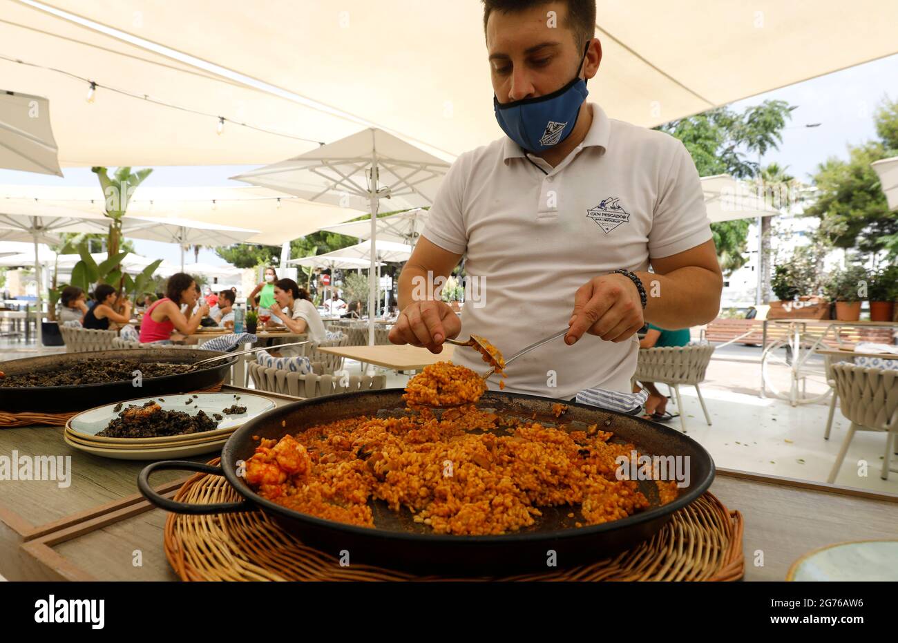 Muro, Spain. 11th July, 2021. The waiter Sebastian serves a paella in the restaurant Can Pescador on the beach Playa de Muro in the north of Mallorca. The federal government has declared the whole of Spain with Mallorca and the Canary Islands in view of rapidly increasing Corona numbers as a risk area. The practical effects for Mallorca holidaymakers are limited for the time being. Credit: Clara Margais/dpa/Alamy Live News Stock Photo
