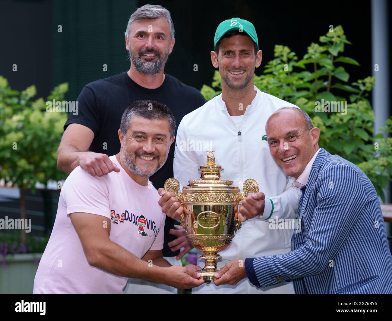 Novak Djokovic and his team, coach Goran Ivanisevic, Edoardo Artaldi, and  Ulises Badio, holding the Gentlemen's Singles Trophy on the players lawn  after the final on day thirteen of Wimbledon at The