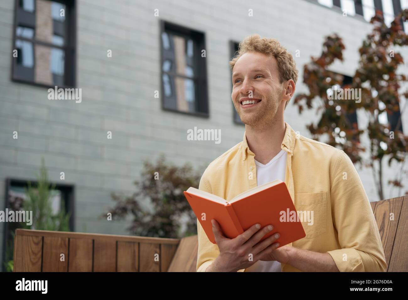 Young smiling student studying, exam preparation, reading book, sitting on bench in university campus Stock Photo