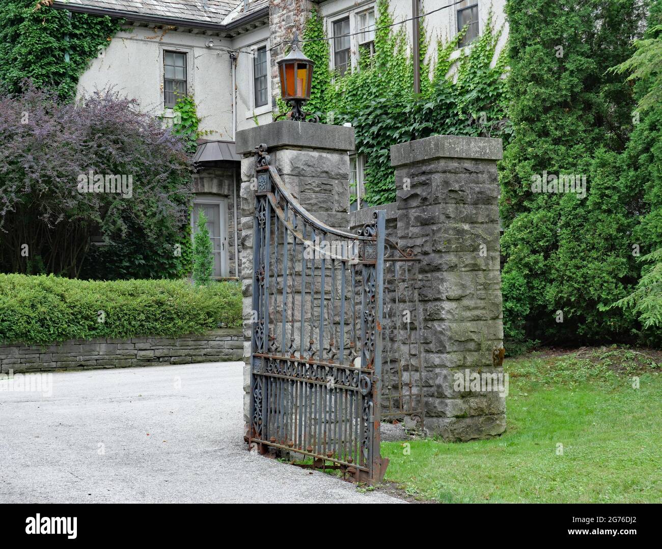 open gate to an old estate house, now rusty and falling off its hinges Stock Photo