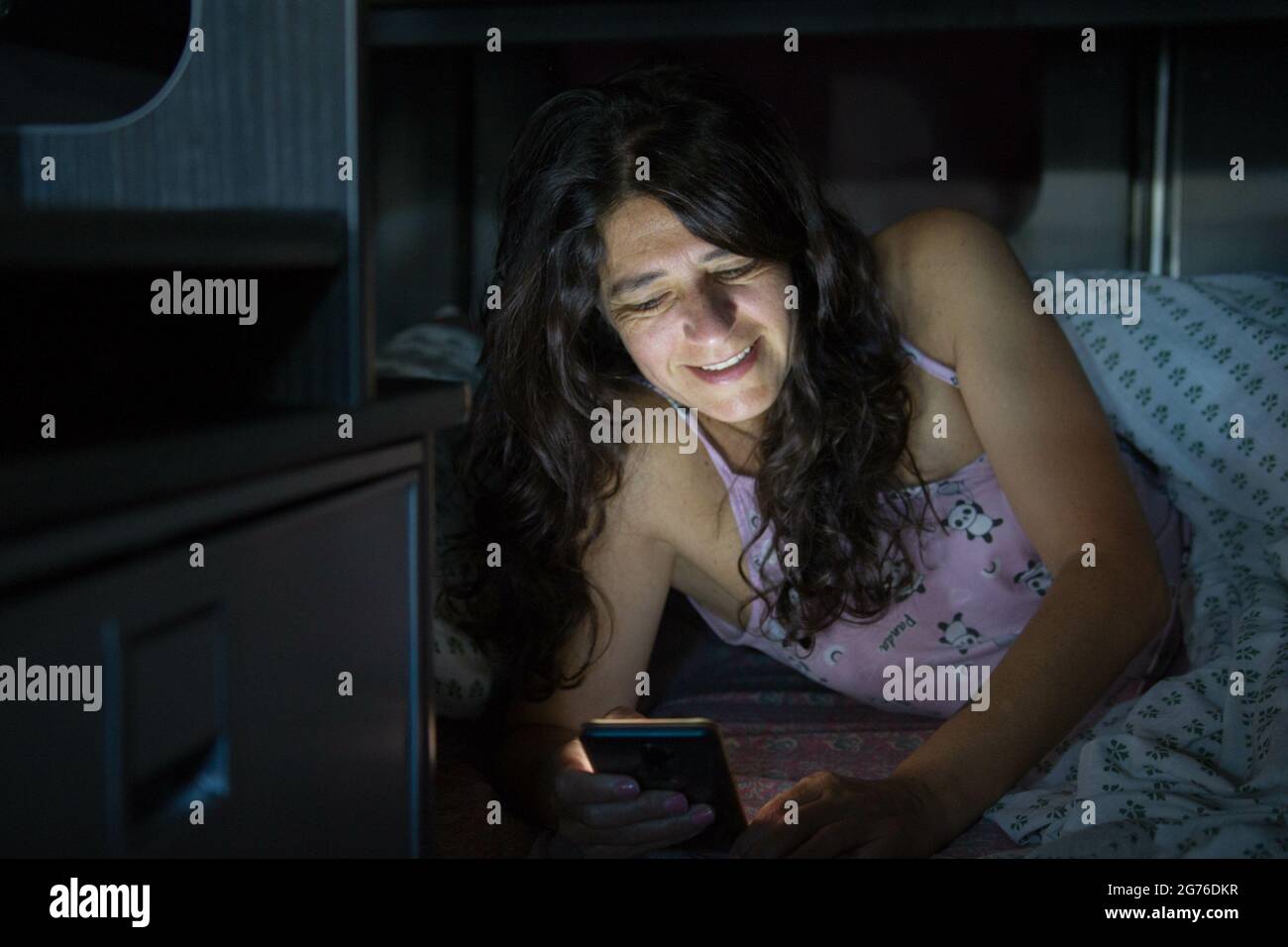 A happy Spanish woman lying on her bed and chatting with her boyfriend
