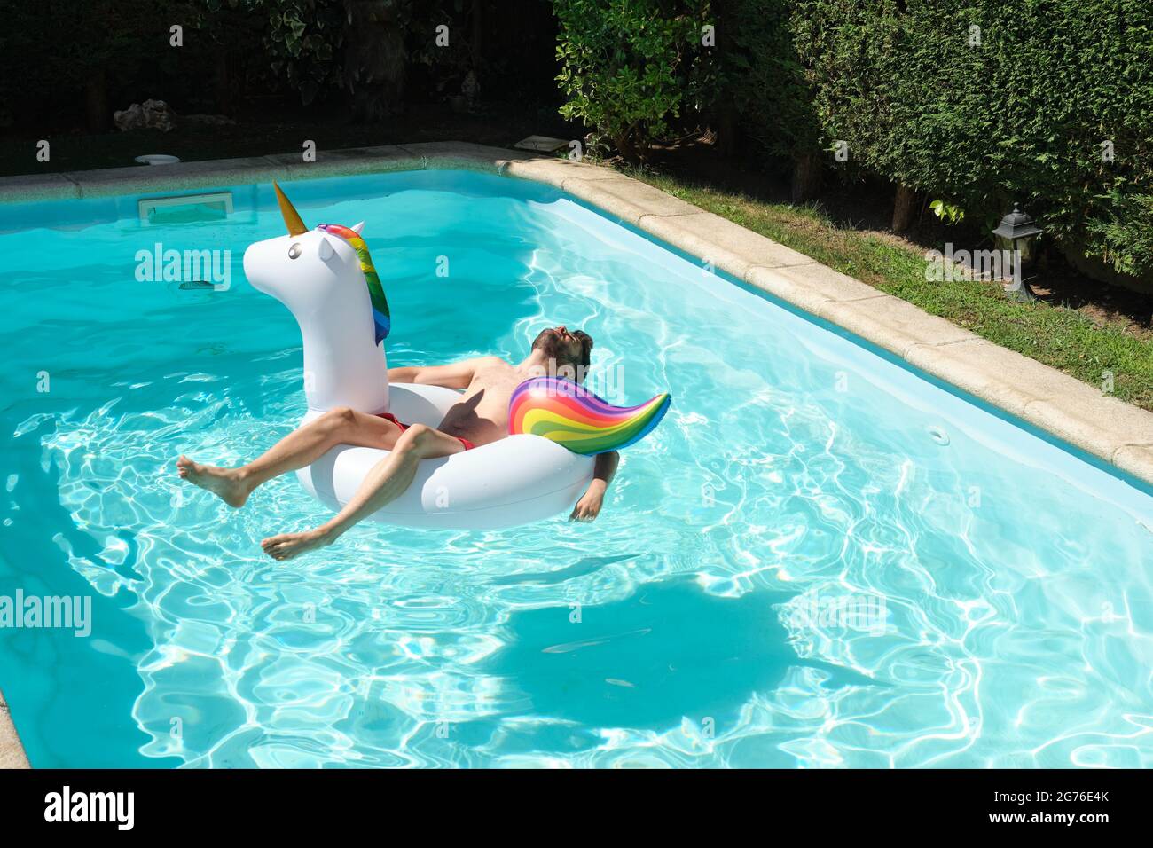 Young man on a big unicorn inflatable ring in a swimming pool. Summer  concept Stock Photo - Alamy