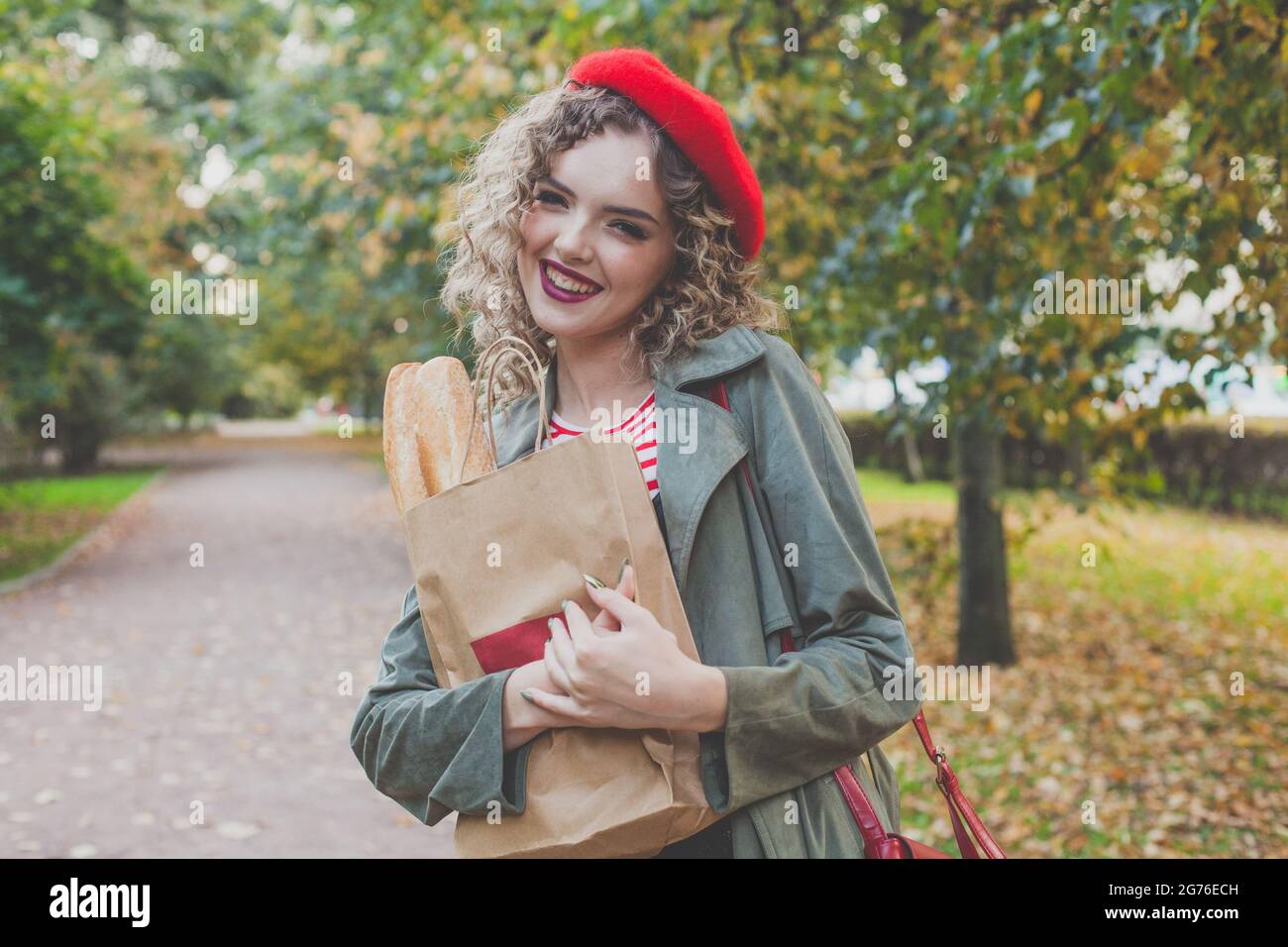 Smiling young woman in red beret holding fresh french baguette outdoor Stock Photo