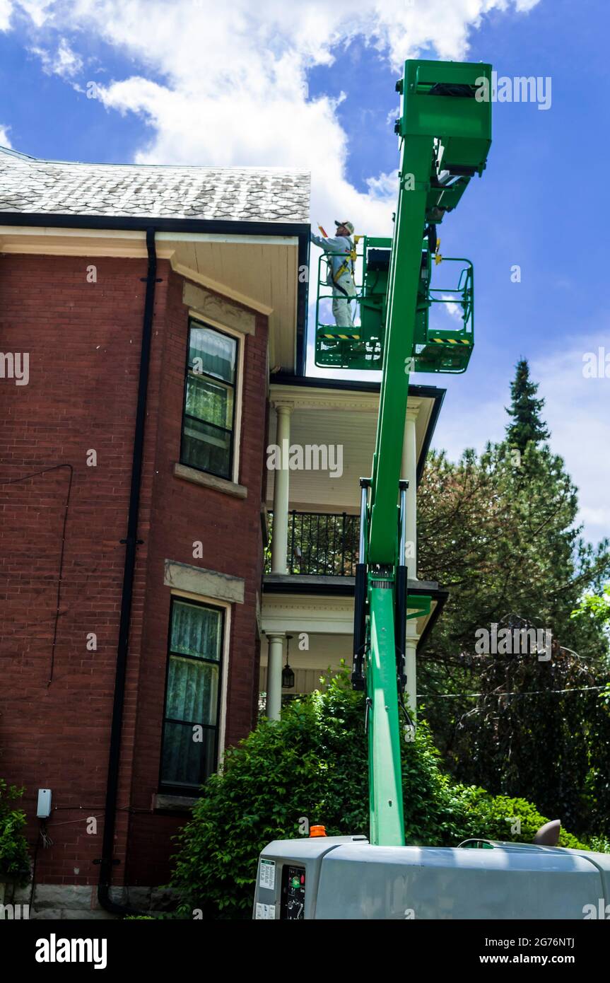 A house painter using a lift is at work on the peak of a tall home, very high lift, Ontario, Canada Stock Photo