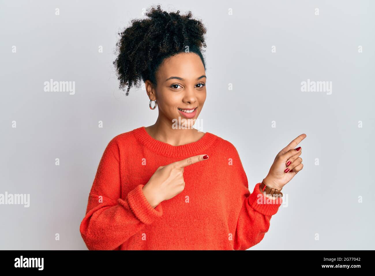 Young african american girl wearing casual clothes smiling and looking at the camera pointing with two hands and fingers to the side. Stock Photo