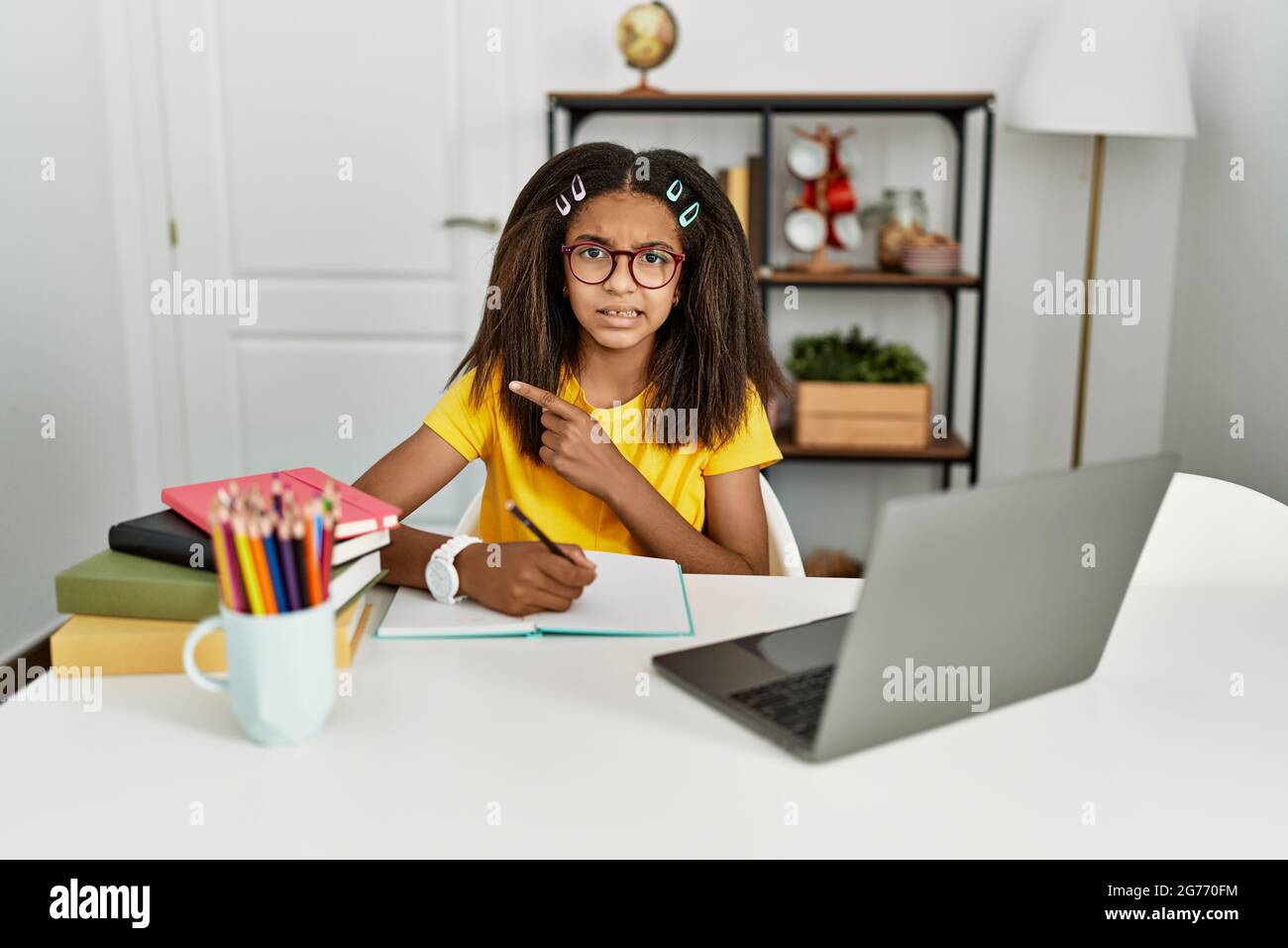 Young african american girl doing homework at home pointing aside ...