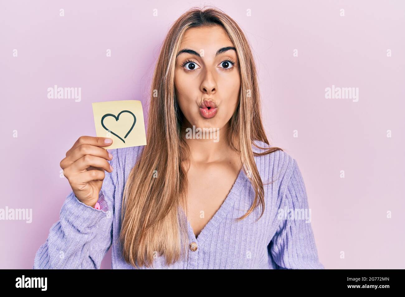 Beautiful Hispanic Woman Holding Heart Reminder Scared And Amazed With Open Mouth For Surprise