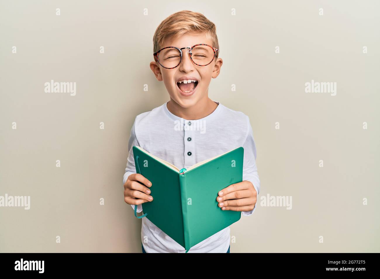 Little caucasian boy kid reading a book wearing glasses smiling and  laughing hard out loud because funny crazy joke Stock Photo - Alamy