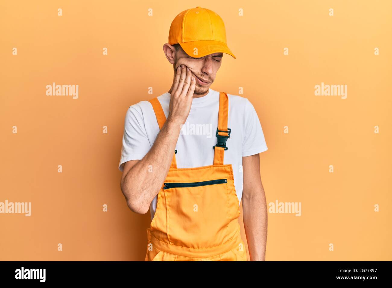 Hispanic young man wearing handyman uniform touching mouth with hand ...