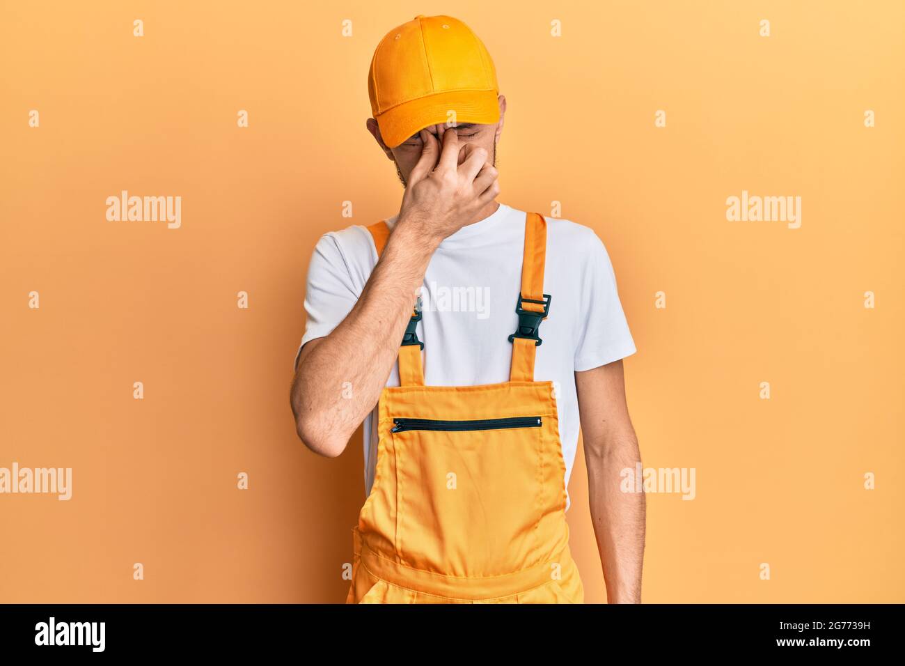 Hispanic young man wearing handyman uniform tired rubbing nose and eyes ...