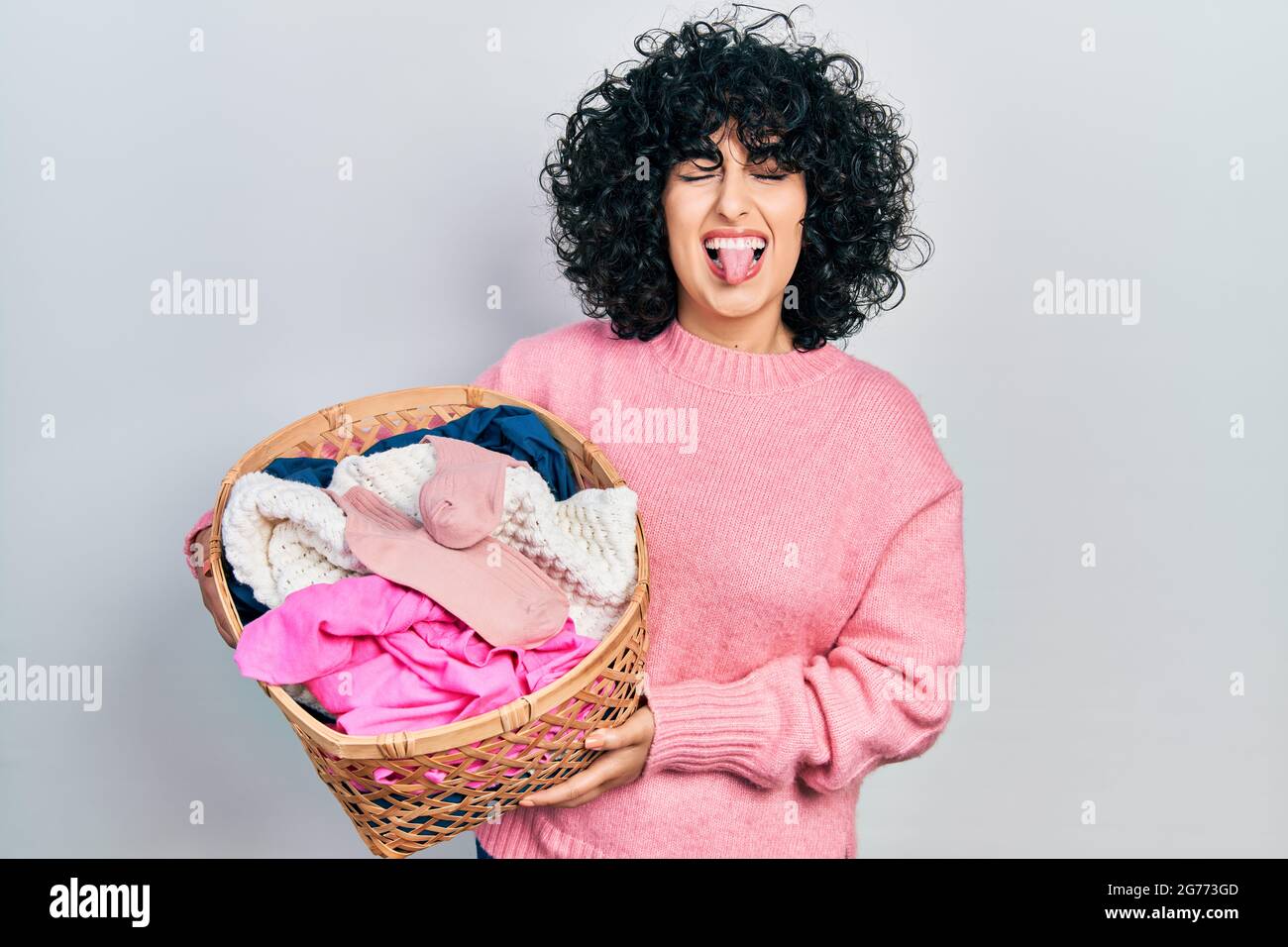 Young middle east woman holding laundry basket sticking tongue out happy  with funny expression Stock Photo - Alamy