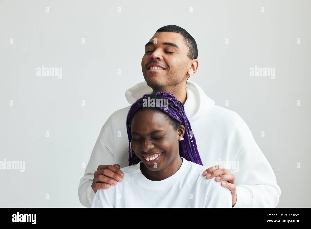Minimal vertical portrait of young mixed-race couple wearing white laughing while posing in studio Stock Photo