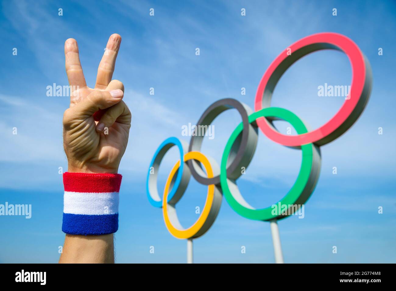 RIO DE JANEIRO - CIRCA MAY, 2016: A hand wearing red white and blue wristband makes a victory sign in front of Olympic Rings Stock Photo
