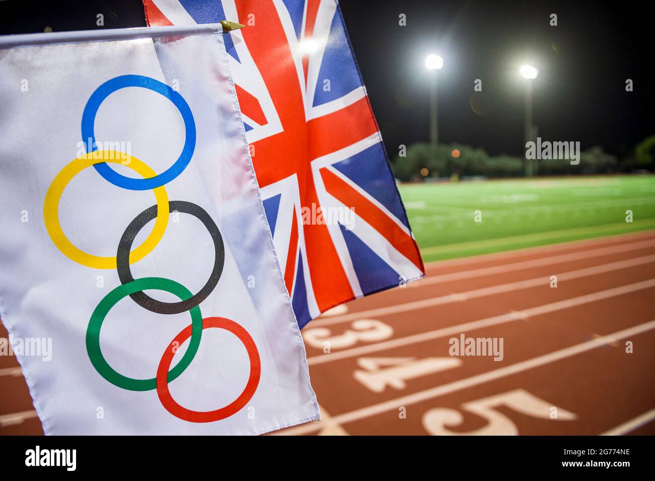 MIAMI, USA - AUGUST 15, 2019: An Olympic and UK Union flag wave together under the floodlights of a red athletics track. Stock Photo