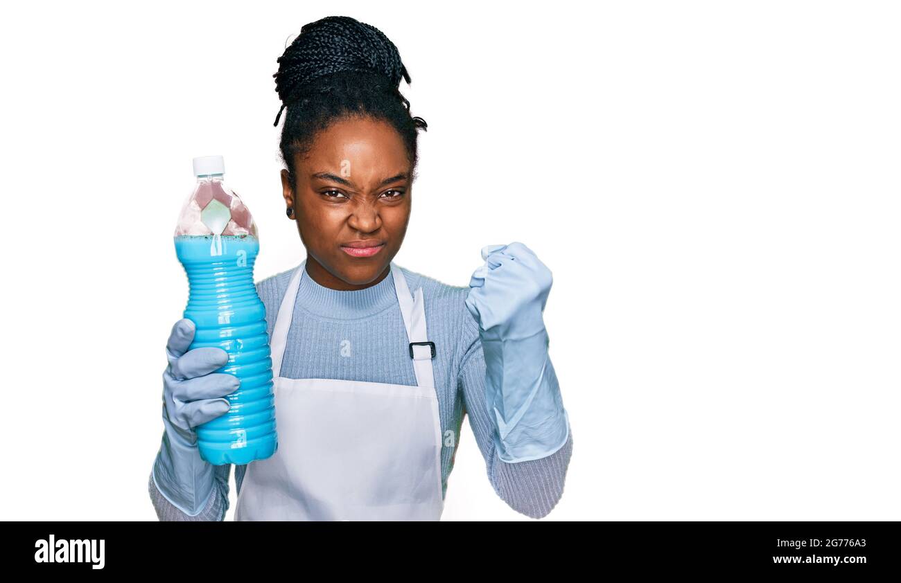 Young african american woman wearing apron holding detergent bottle annoyed and frustrated shouting with anger, yelling crazy with anger and hand rais Stock Photo