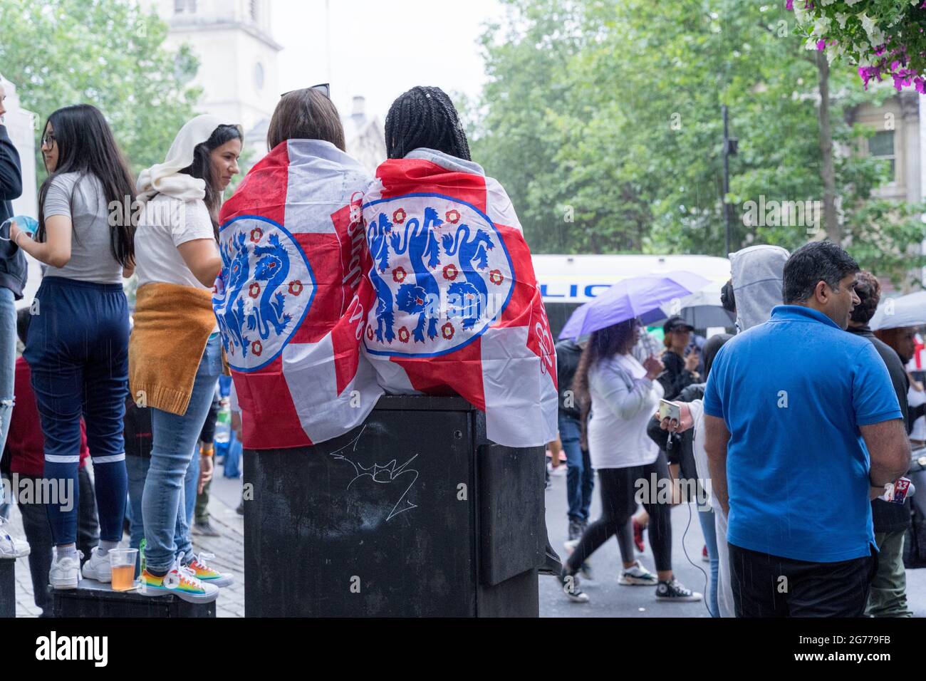 two women wrapped in three lions flags among  football fans singing congregate in central London, England, UK Stock Photo