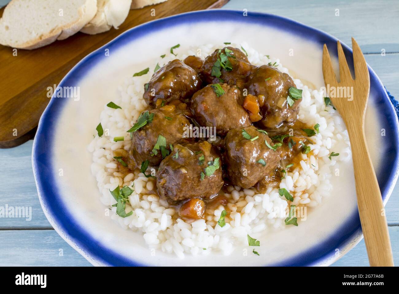 Closeup image of rice with saucy meat and greens on top in the  plate and a wooden fork on it Stock Photo