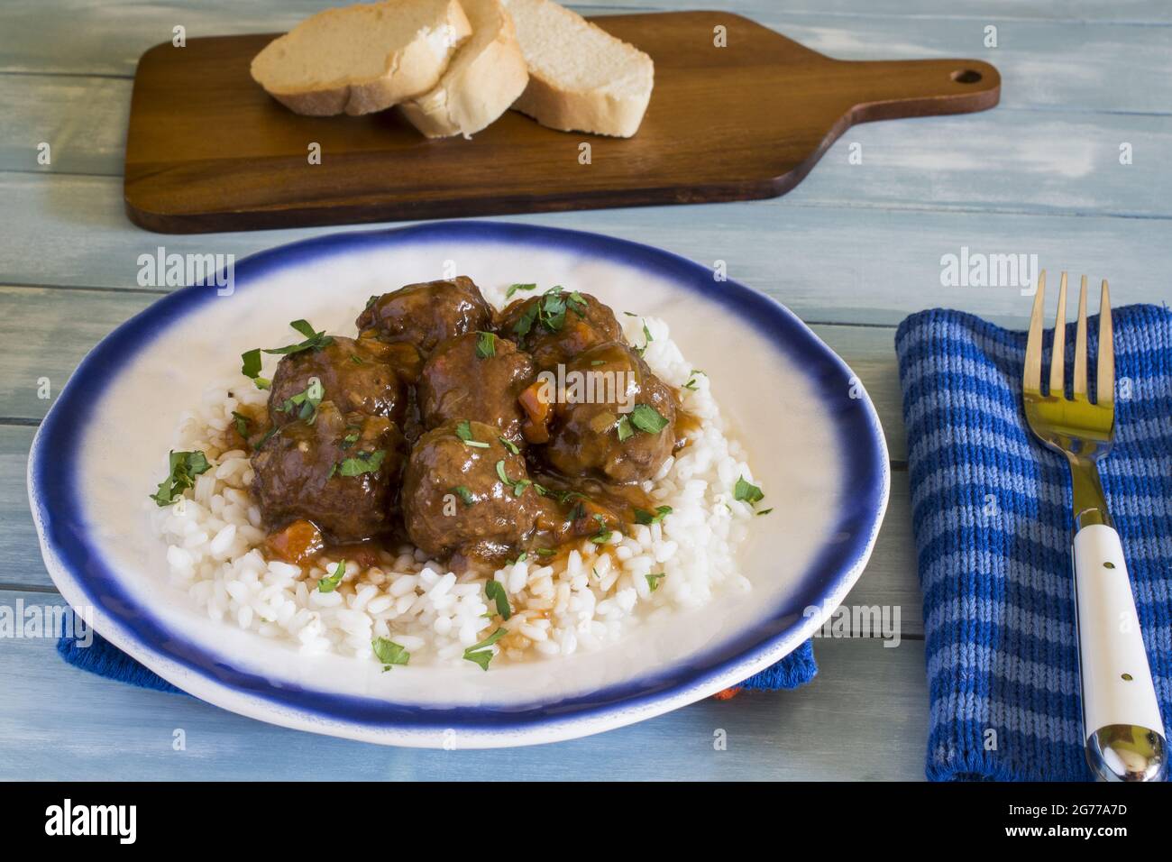 Closeup image of rice with saucy meat and greens on top in the plate and a fork on it with bread Stock Photo