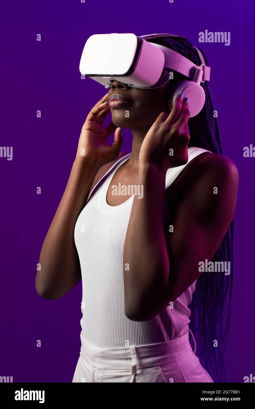 Vertical futuristic portrait of young African-American woman wearing VR headset against purple background Stock Photo