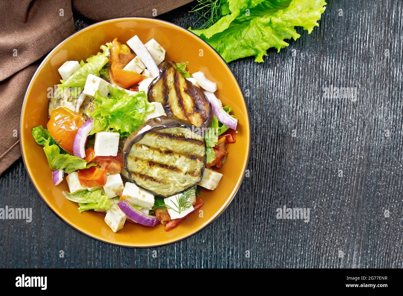 Salad of fried eggplant, fresh tomato, lattuk with red onion and salted feta cheese, seasoned with vegetable oil and soy sauce in a plate, napkin and Stock Photo