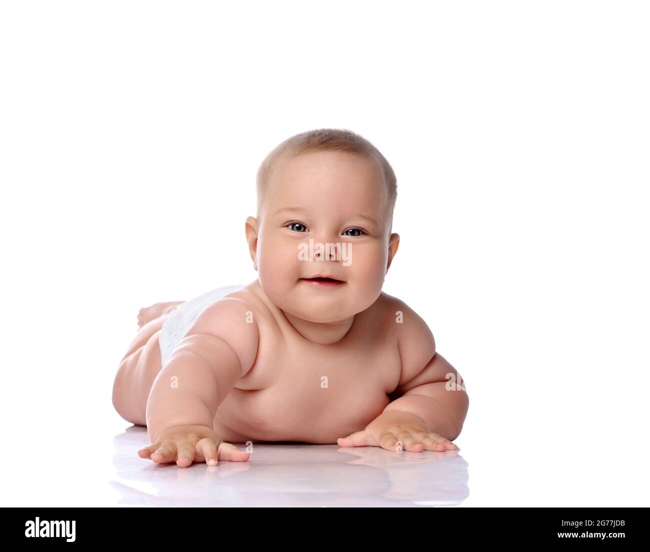 Playful infant child baby girl kid in diaper is lying on her stomach trying to reach, touch camera, slapping on floor  Stock Photo