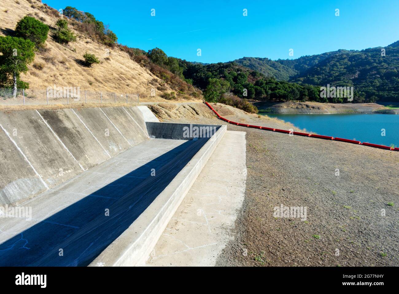 Concrete dam spillway, orange debris boom on dry ground. Extremely low water level in drying during summer Stevens Creek reservoir in San Francisco Ba Stock Photo