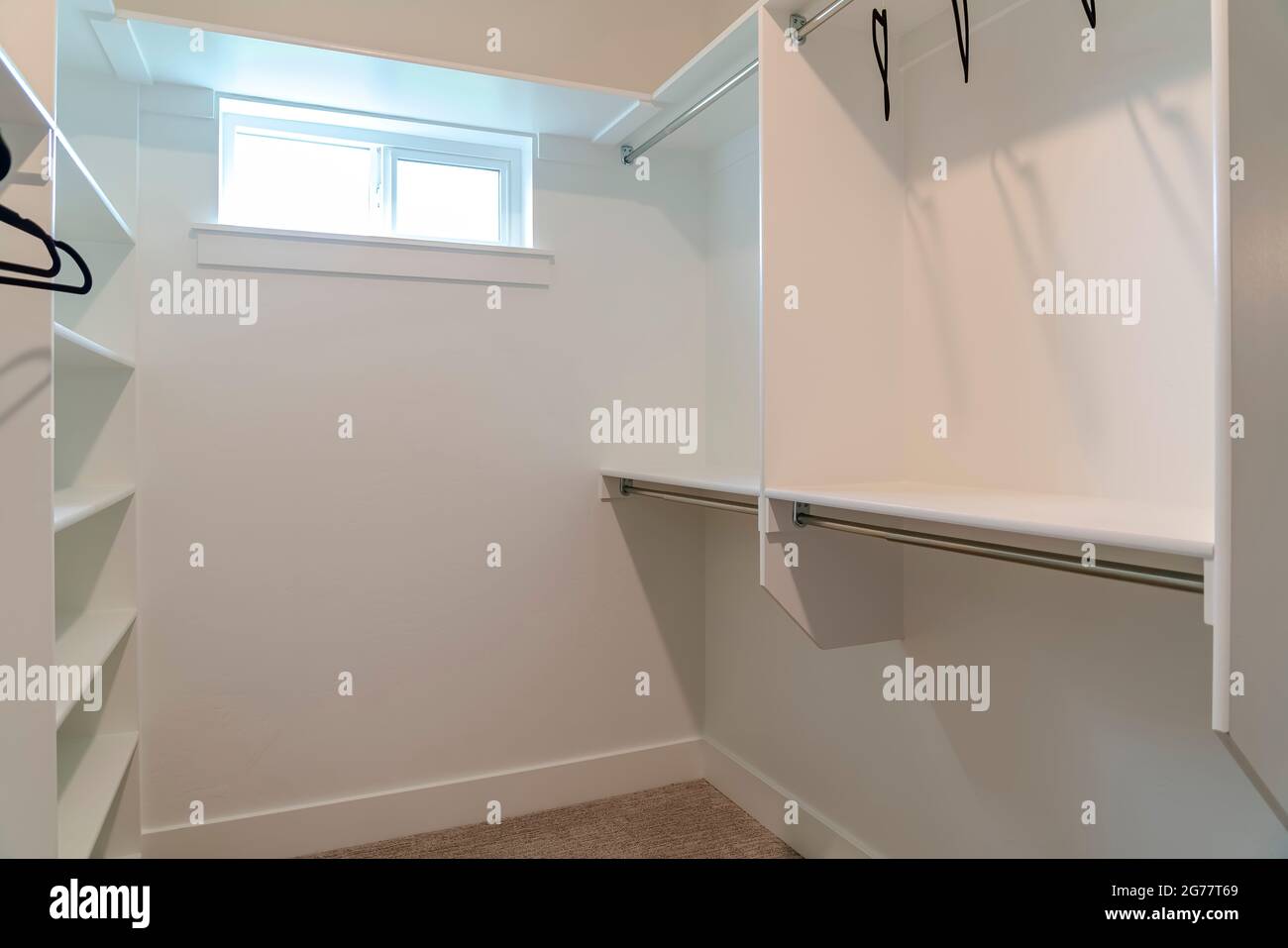 Walk in closet of a new home with empty wall shelves and garments rods ...