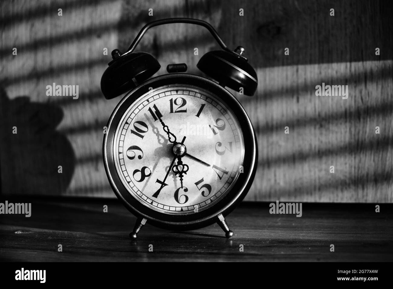 Retro alarm clock early morning on table rays sunlight through blinds