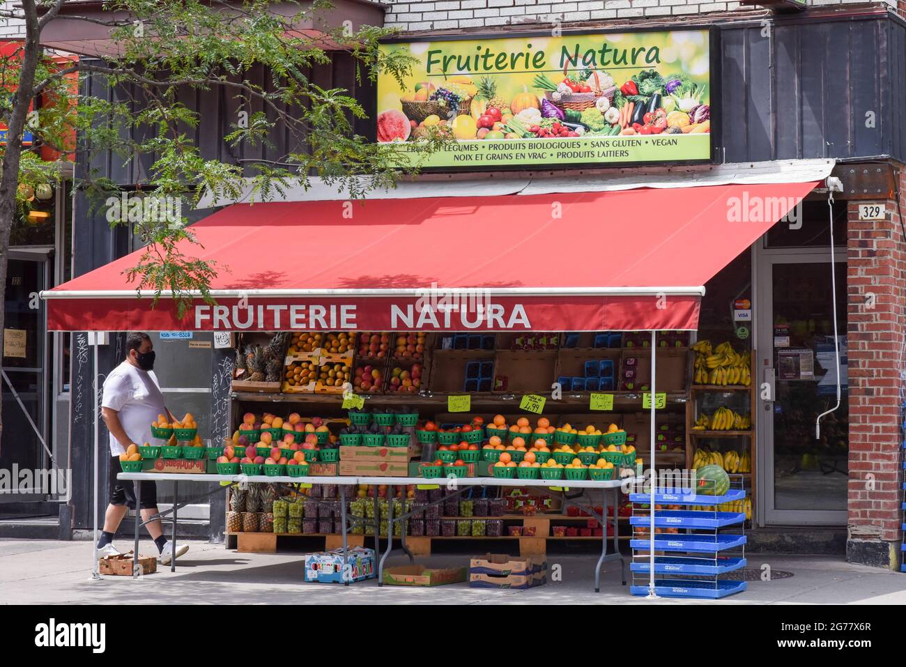 Person wearing a mask walking in front of vegetable store, Montreal Canada Stock Photo