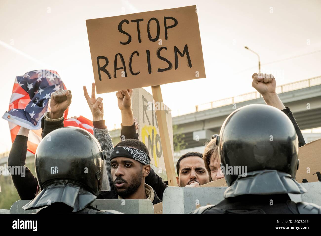Group of displeased young American people raising fists and banner while asking to stop racism, police keeping crowd Stock Photo